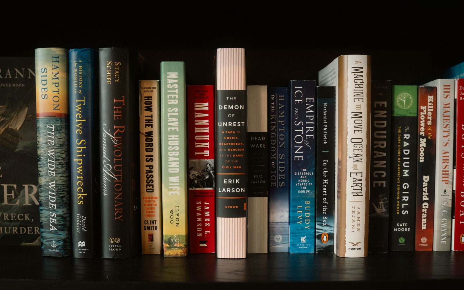 Row of hardcover nonfiction history titles standing upright on a dark wooden shelf