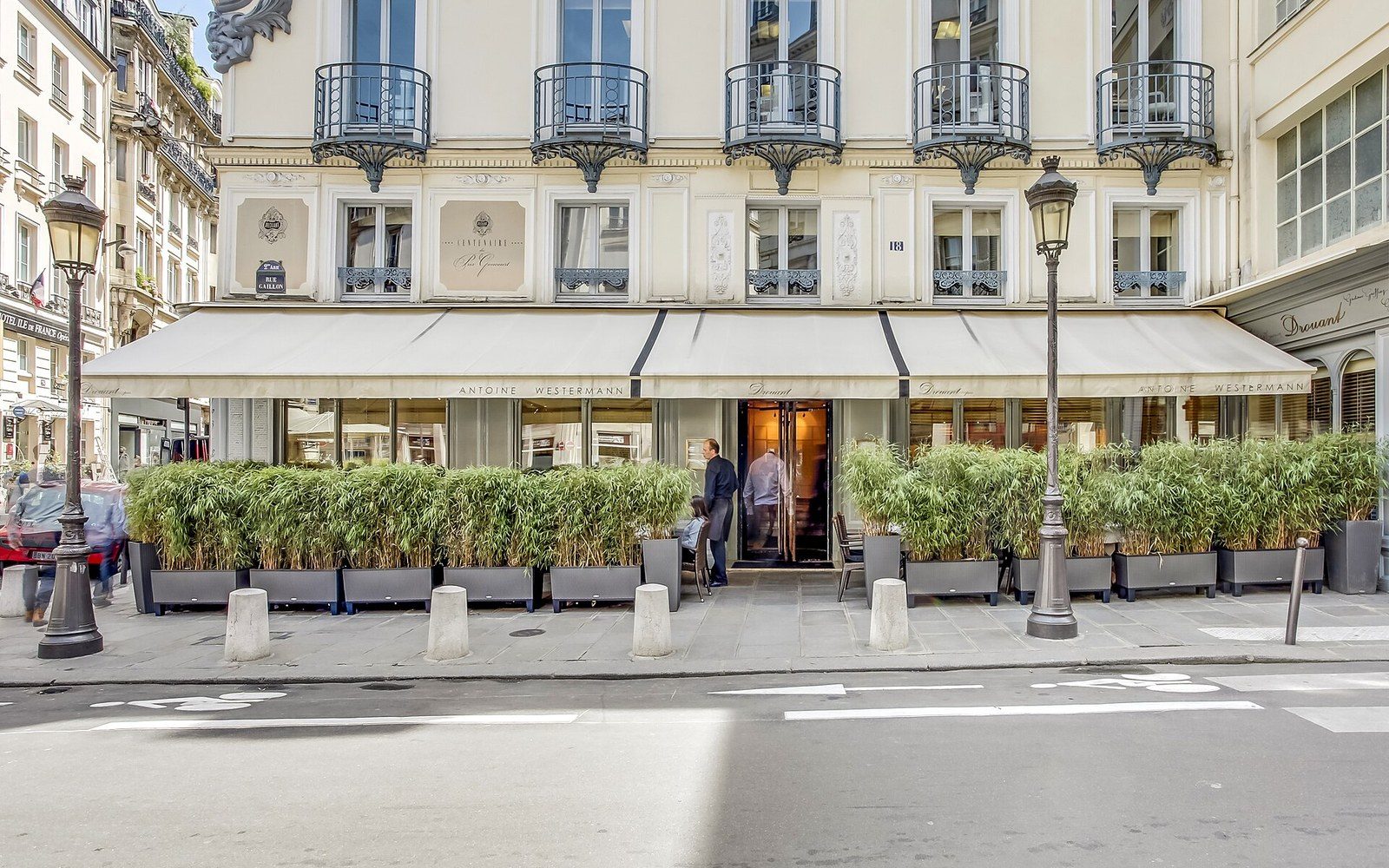 Restaurant Drouant's cream awnings and iron balconies front a Paris street with potted bamboo hedges