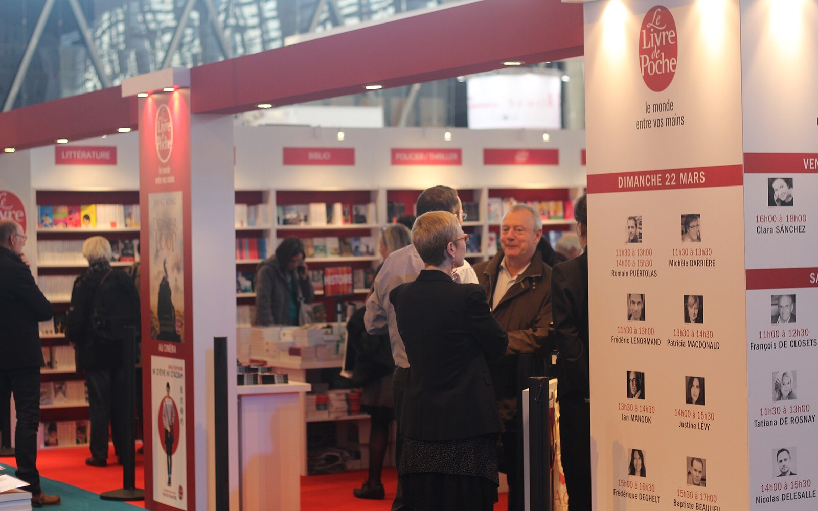 Visitors browse the Le Livre de Poche booth at a book fair with author signing schedules displayed