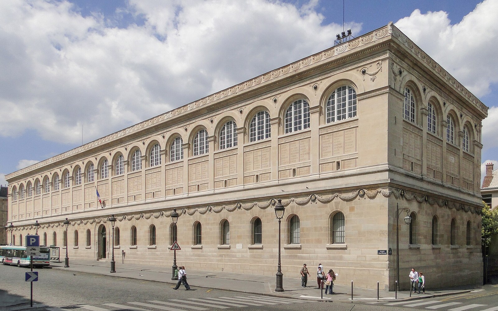 Long stone façade of the Bibliothèque Sainte-Geneviève with rows of arched windows facing a street corner