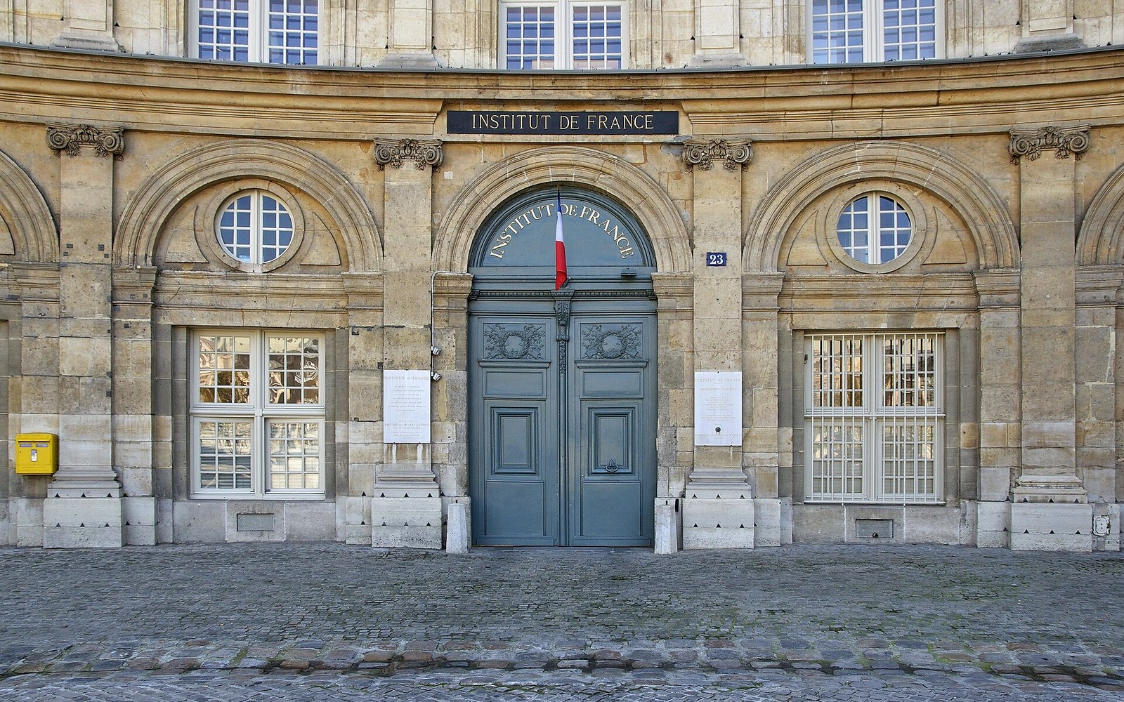 Arched entrance of the Institut de France with a French flag above blue doors