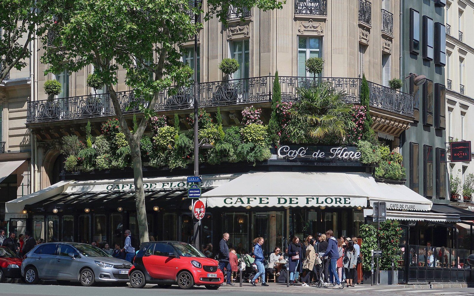 Café de Flore's corner terrace on a Paris boulevard, crowded with patrons under striped awnings