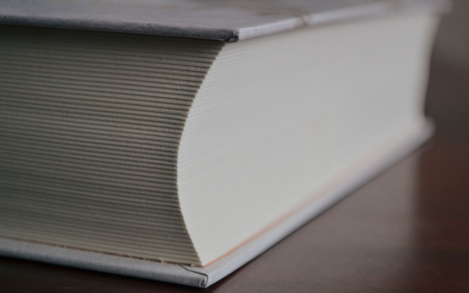 Close-up of a thick book's closed pages showing the edge and corner on a wooden surface