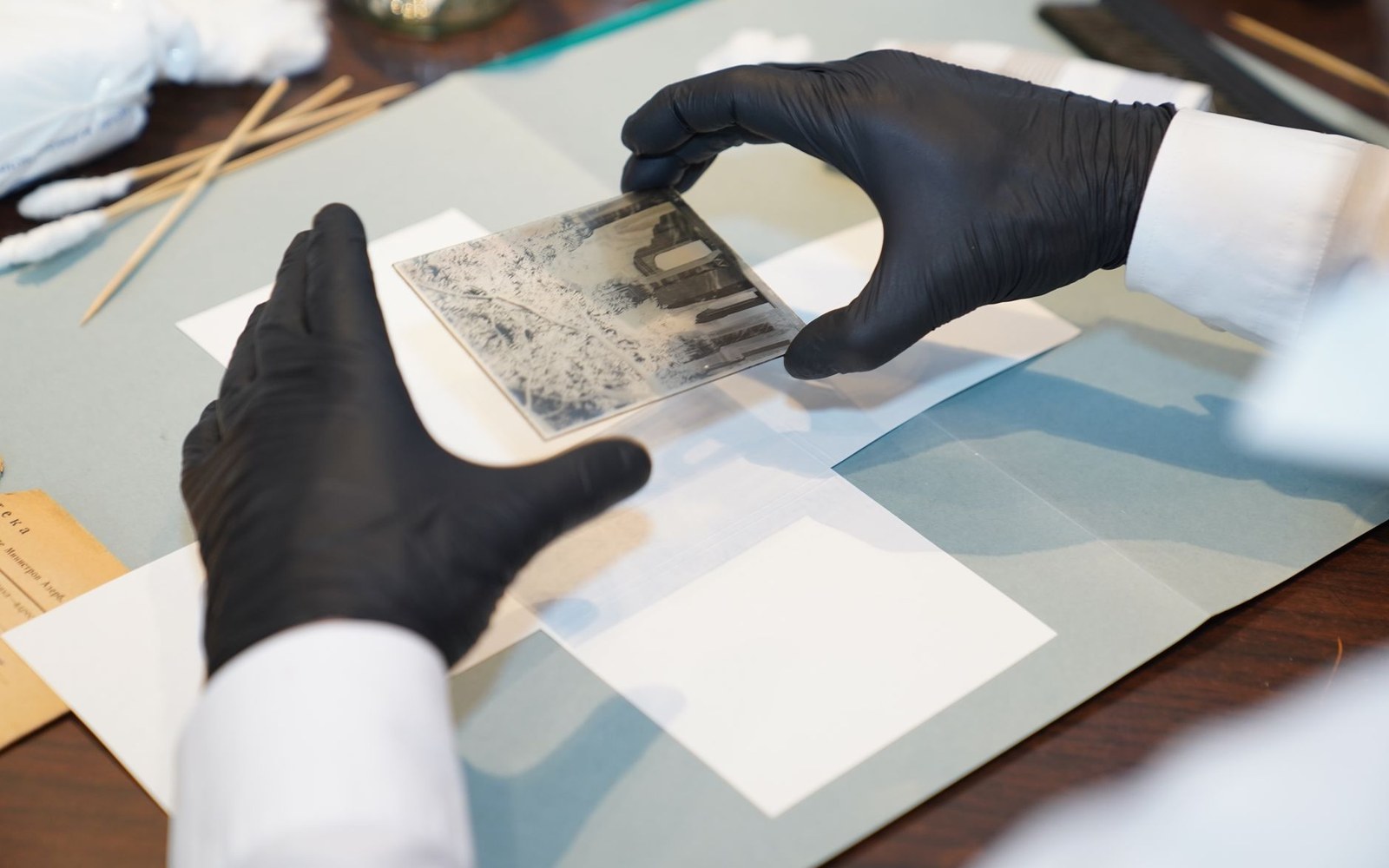 A handwritten manuscript page under conservation glass at the BnF, the ink and corrections of the author visible in raking light, an archivist's gloved hands at the edge of the frame