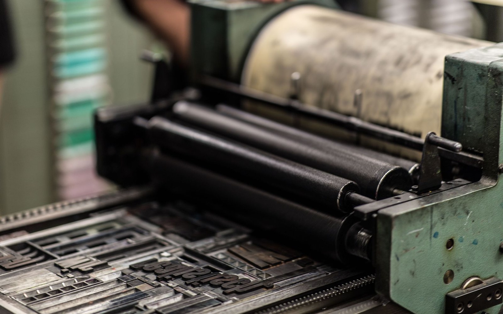 A printer's forme of moveable French type locked in its chase, the lead letters in close-up, a compositor's hand steadying the quoin at the frame's left edge