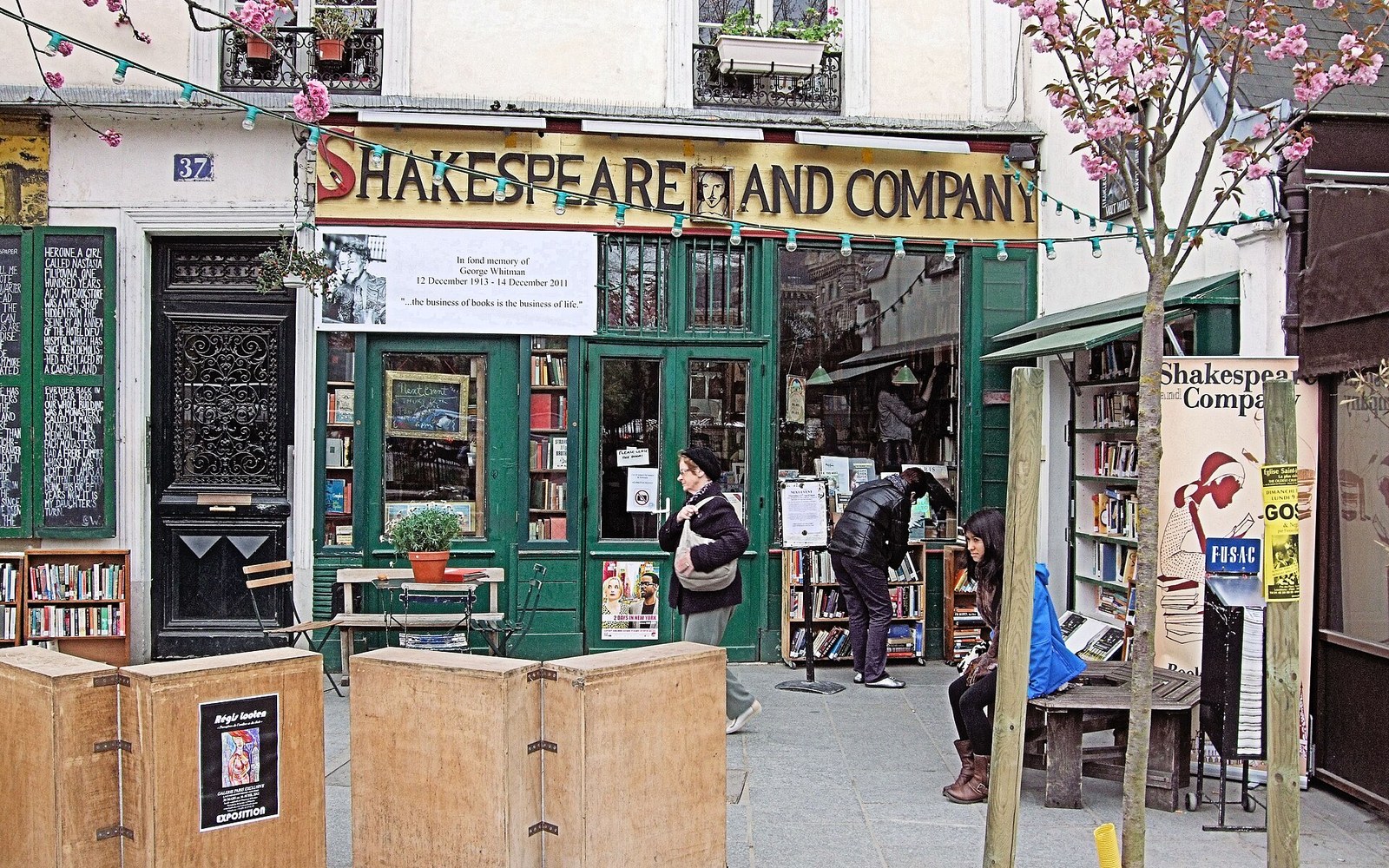 The shopfront of Shakespeare and Company at 37 rue de la Bûcherie, its yellow sign and stacked books in the window, the street of the Latin Quarter visible behind
